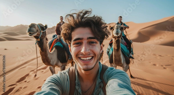 Obraz A man taking a selfie in the desert with a group of people on camels behind him, a happy and smiling man 