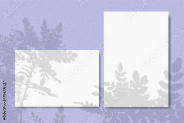 Fototapeta Horizontal and vertical sheets of white textured paper against a violet wall background. Natural light casts shadows from a branch of tropical plants. Mock up