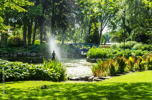 Fototapeta Park with water fountain and a statue in a pond.
