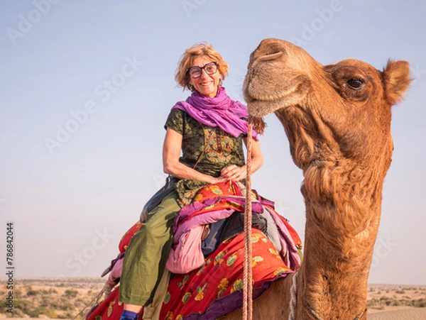 Fototapeta Joyful tourist riding camel in Jaisalmer desert