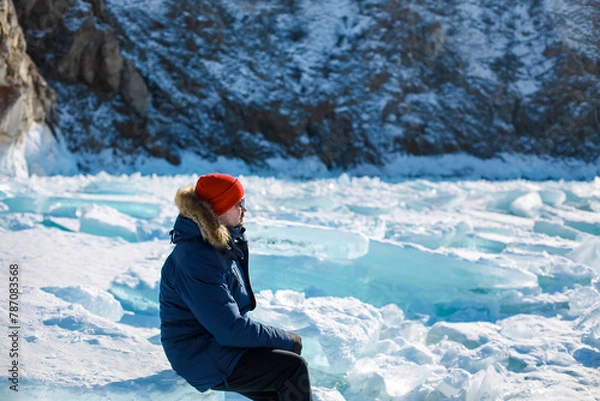 Fototapeta Portrait of the man tourist in red cap and blue jacket wearing sunglasses on ice
