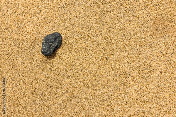 Fototapeta single black stone in a fine sand at the beach