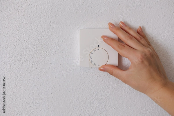Fototapeta Human hand turns off the heating at home. Central Heating thermostat control dial adjustment. Place for text. Woman turning down heating thermostat to save money.