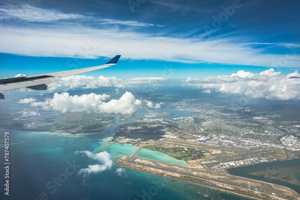 Fototapeta "Above the Horizons: An aerial vista captures Oahu, Hawaii, with the airport below, framed by billowing clouds, a vast expanse of blue sky, and the distant shimmer of ocean waters"