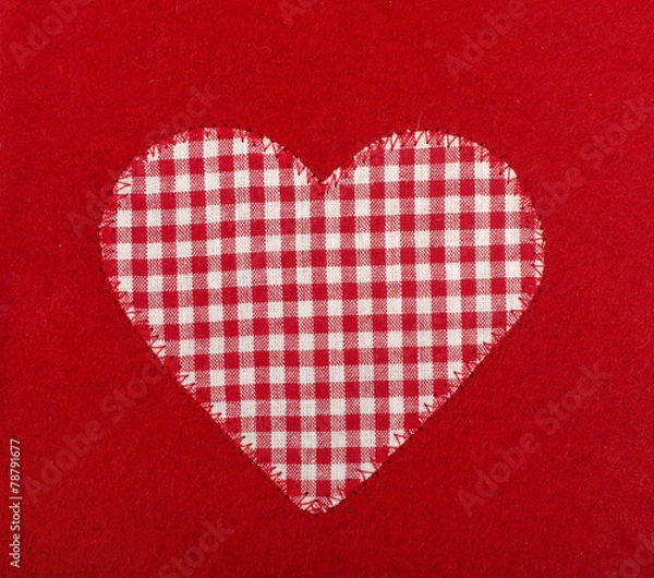 Obraz Checkered heart shape sewed on red wool background.