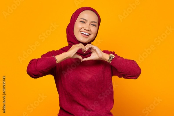 Fototapeta Smiling young girl in red sweater showing heart with two hands,