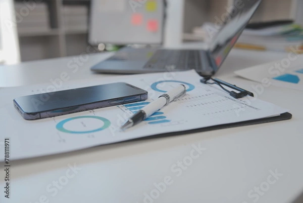 Fototapeta Close up view of simple workspace with laptop, notebooks, coffee cup and tree pot on white table with blurred office room background