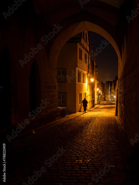 Obraz Person walking the streets of Rothenburg ob der Tauber at night, framed by an archway