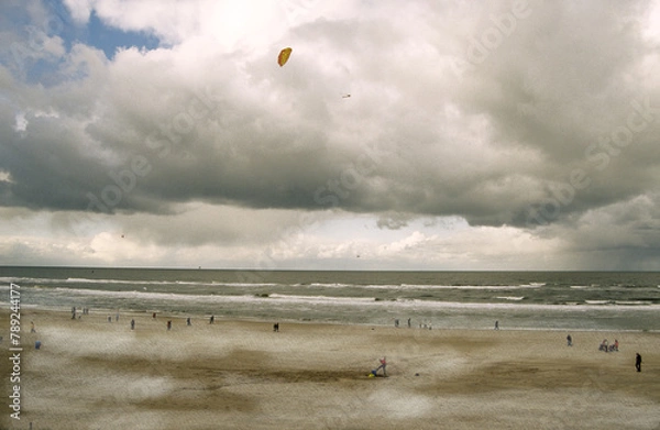 Fototapeta Stormy sky with clouds. Beach scene with flying kite. and miniature view of people on the sands. Thornham Beach Norfolk UK 2003