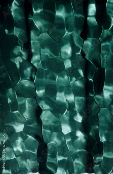 Fototapeta vertical image of sunlight shining through green window glass. reflecting shades of colour with a dappled effect