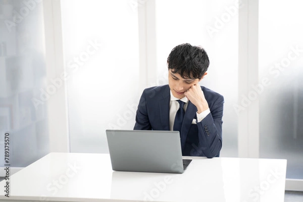 Obraz ノートパソコンで資料作成時に悩む男性ビジネスマン