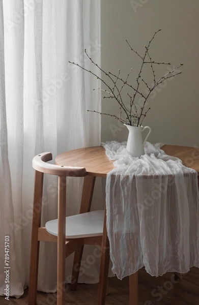 Fototapeta The simple interior of the living room - a round wooden table with a jug with branches and a chair. Minimalism style