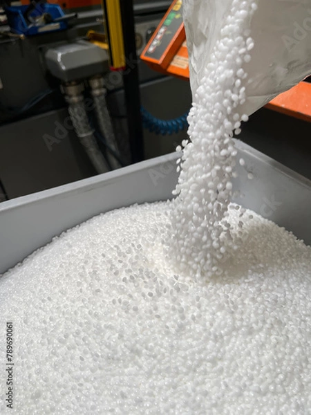 Obraz pouring of a bag of white plastic pellets on a gray plastic drawer, production of plastic parts, plastic injection, spilling of plastic pelets, with a plastic injector out of focus in the background, 