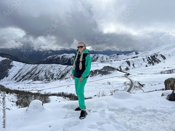 Fototapeta A woman on the background of the Ceylomsky pass in Ingushetia. A trip uphill to the Tsei Lum pass on a cloudy spring day. Panorama of the high cliffs of the Dzheyrakh gorge
