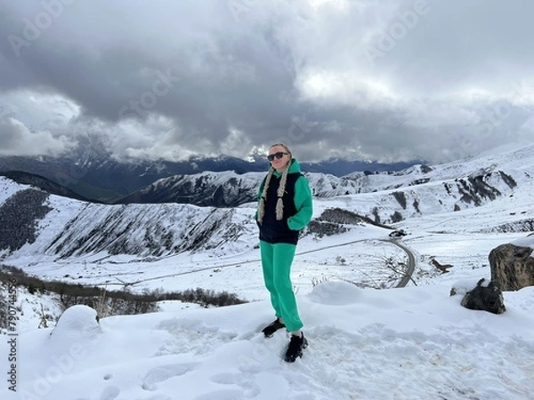 Fototapeta A woman on the background of the Ceylomsky pass in Ingushetia. A trip uphill to the Tsei Lum pass on a cloudy spring day. Panorama of the high cliffs of the Dzheyrakh gorge