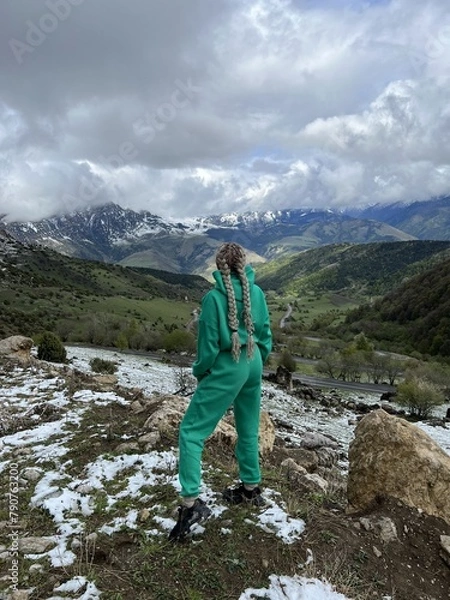 Fototapeta A woman on the background of the Ceylomsky pass in Ingushetia. A trip uphill to the Tsei Lum pass on a cloudy spring day. Panorama of the high cliffs of the Dzheyrakh gorge