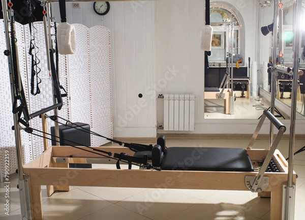 Fototapeta Woman training pilates on the reformer bed. Reformer pilates studio machine for fitness workouts in gym. Fit, healthy and strong authentical body. Fitness concept