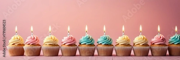 Fototapeta Colorful cupcakes with lit candles are displayed against a pink background, indicating an indoor celebration event marking of joy and celebrating. with free space