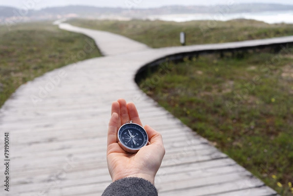 Fototapeta A person holding a compass on a wooden boardwalk. The promenade has two paths.