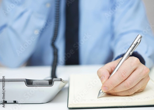 Fototapeta Businessman is talking on the phone and writing memo