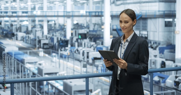 Fototapeta Portrait of a Beautiful Happy Engineer Using Laptop Computer and Looking Around a Factory Facility with Automated Robotic Arms Producing Modern Electronic Components for Different Industries