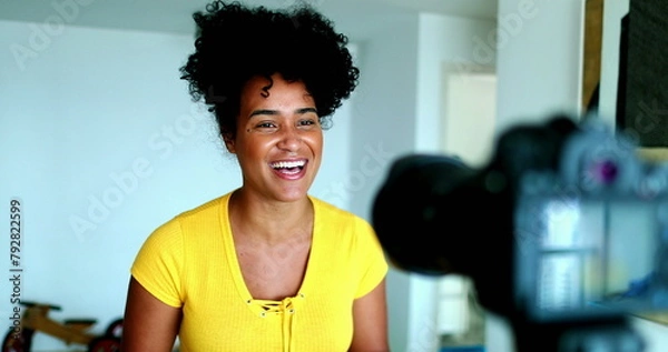 Fototapeta One young black woman speaking in front of camera giving testimony for online channel. 20s female vlogger creating video post engaged with new media