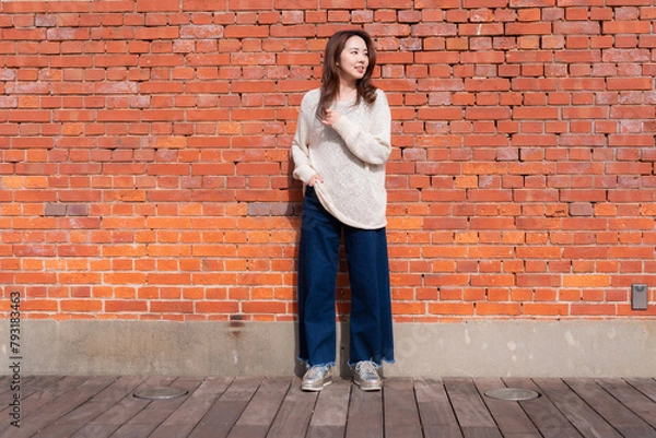 Fototapeta レンガの塀の前でポーズをとる女性