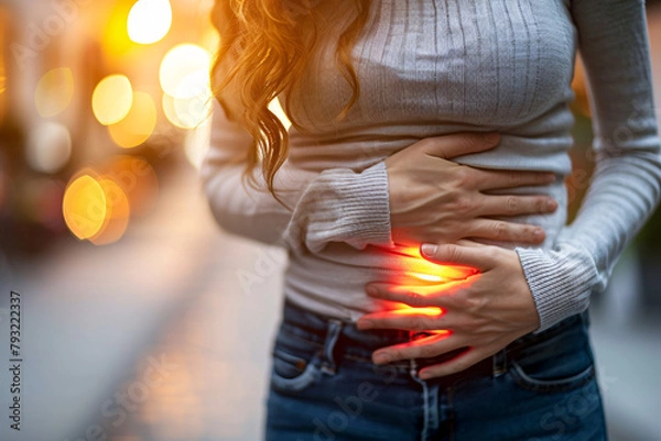 Fototapeta A woman with gastrointestinal complaints and stomach pain standing outside in nature