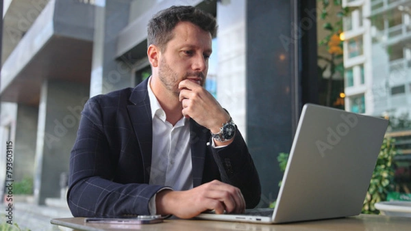 Obraz Handsome 30s top manager work laptop. Entrepreneur type computer macbook. Business man look monitor. Young male businessman. Urban city background. 40s employee create start up. Ceo office boss job.