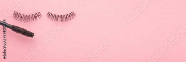 Fototapeta Dark black false lashes and eye mascara on light pink table background. Pastel color. Female beauty product. Closeup. Wide banner. Empty place for text. Top down view.