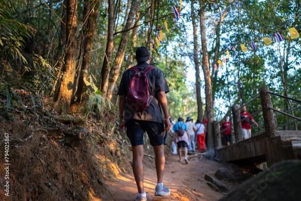 Obraz Asian tourists are walking up Khao Khitchakut, through large trees in the forest, tourist attraction Chanthaburi, Thailand.