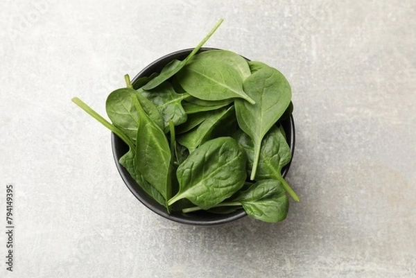 Fototapeta Fresh spinach leaves in bowl on light textured table, top view
