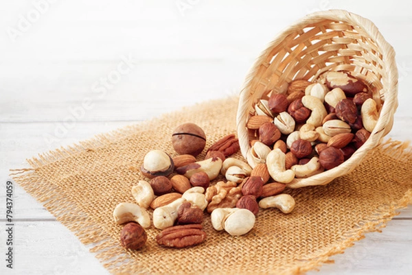 Fototapeta Nuts Mix in a Wooden Plate on a White Background. Wicker Basket full of Cashew, Walnuts, Hazeltuts, Peanuts, Brazilian Nuts, Pistachios on a Burlap with Side View