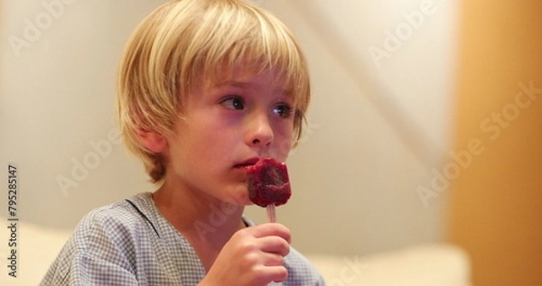 Obraz Small boy eating ice cream dessert while watching TV screen at home after dinner