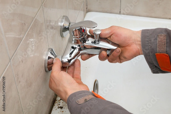 Fototapeta Plumber works in a bathroom replacing faucet, tap