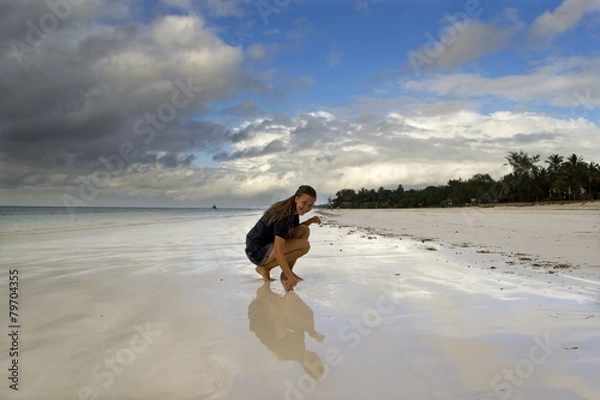 Obraz Young woman sitting on beach with reflective sand