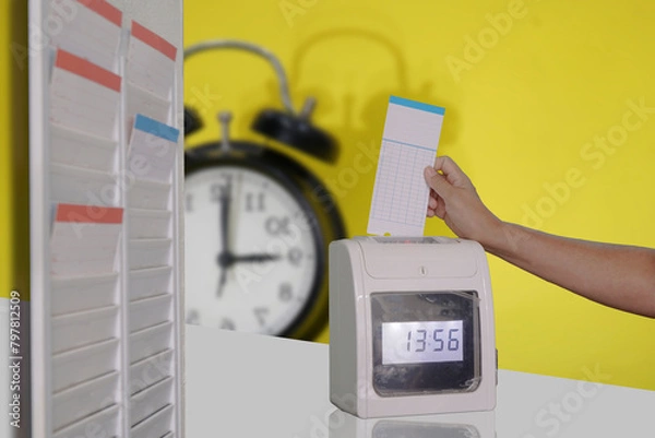 Fototapeta A time clock with a clock behind it and a hand punching in.