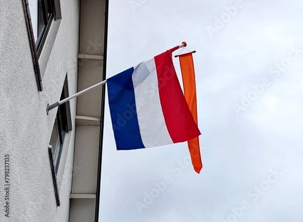 Fototapeta National red white blue colored flag of the Netherlands hangs on a flagpole on a house in a residential area because of the celebration of King's Day (Dutch culture)