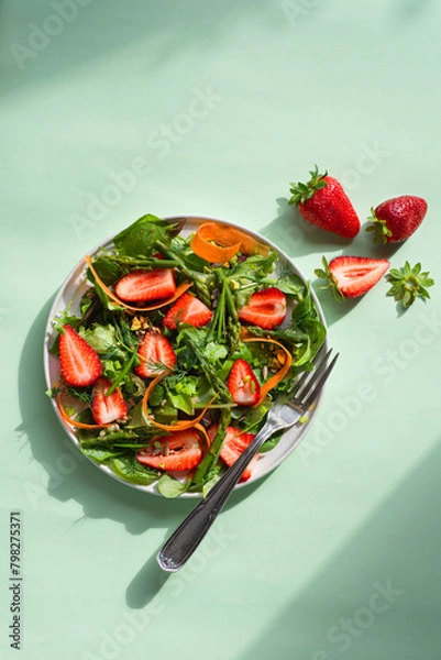 Fototapeta Spring light salad with strawberries, asparagus, carrots, arugula leaves, spinach and flax seeds, nuts and olive oil dressing. Light salads with fruits and berries, sweet and salty taste, dietary bala