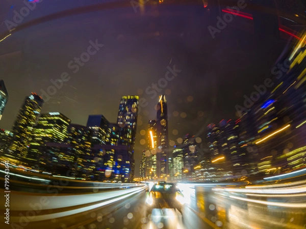 Fototapeta Back car window view of long exposure of the highway in the city. City at night Driving a car, the city at night. Camera at the vehicle back trunk glass. Rainy night soft glowing.