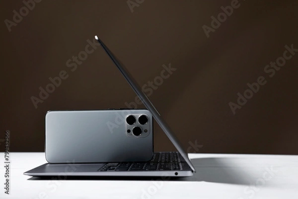 Fototapeta Modern laptop and smartphones on white table against brown background. Space for text
