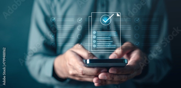 Fototapeta quality, management, check, compliance, list, marketing, information, social, network, system. A man is holding a smartphone with a check mark on it. Concept of accomplishment or satisfaction.