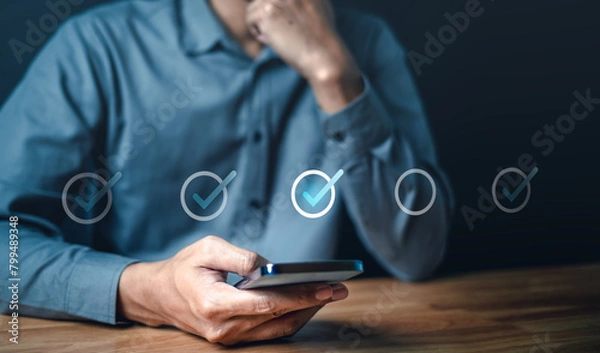 Fototapeta social, marketing, touch, information, corporate, network, office, finance, smartphone, media. A man is holding smartphone and looking at a screen with check mark. as like completed or approved.