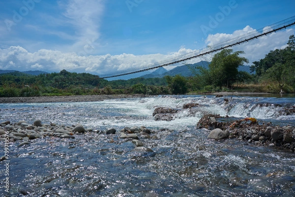 Fototapeta Sabahan hanging bridge over the Melangkap river with background of mountain range. Scene from Tegudon Tourism Village.