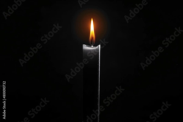 Fototapeta A tall candle burning with a soft light on a dark background