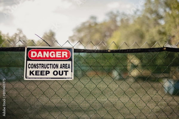 Obraz Danger Construction area sign hanging on a chain link fence at a construction site,  horizontal, side space