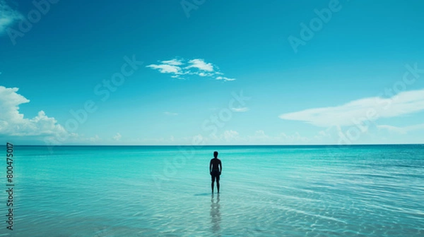 Fototapeta Clear turquoise waters invite a solitary figure wading with a beautiful blue sky overhead and a whisper of clouds