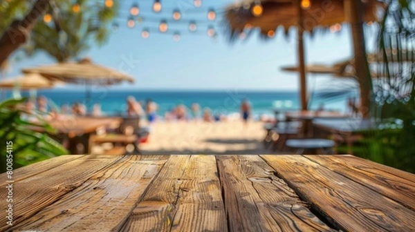 Obraz An empty wooden table with a blurred beach party in the background, setting the stage for summer gatherings.