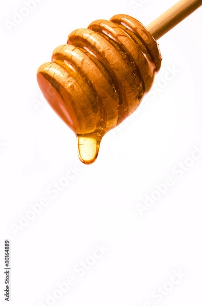 Fototapeta Honey dripping from a wooden honey dipper isolated on white