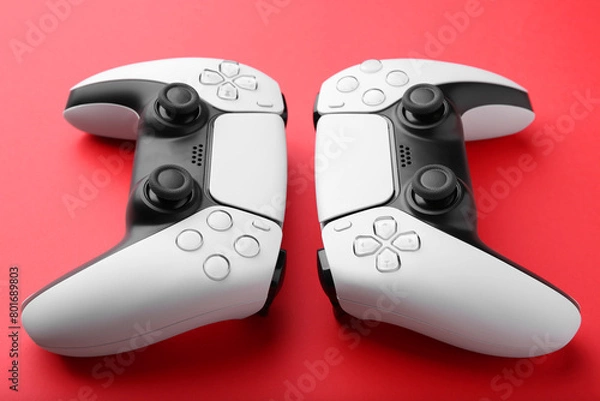 Fototapeta Two wireless game controllers on red background, closeup
